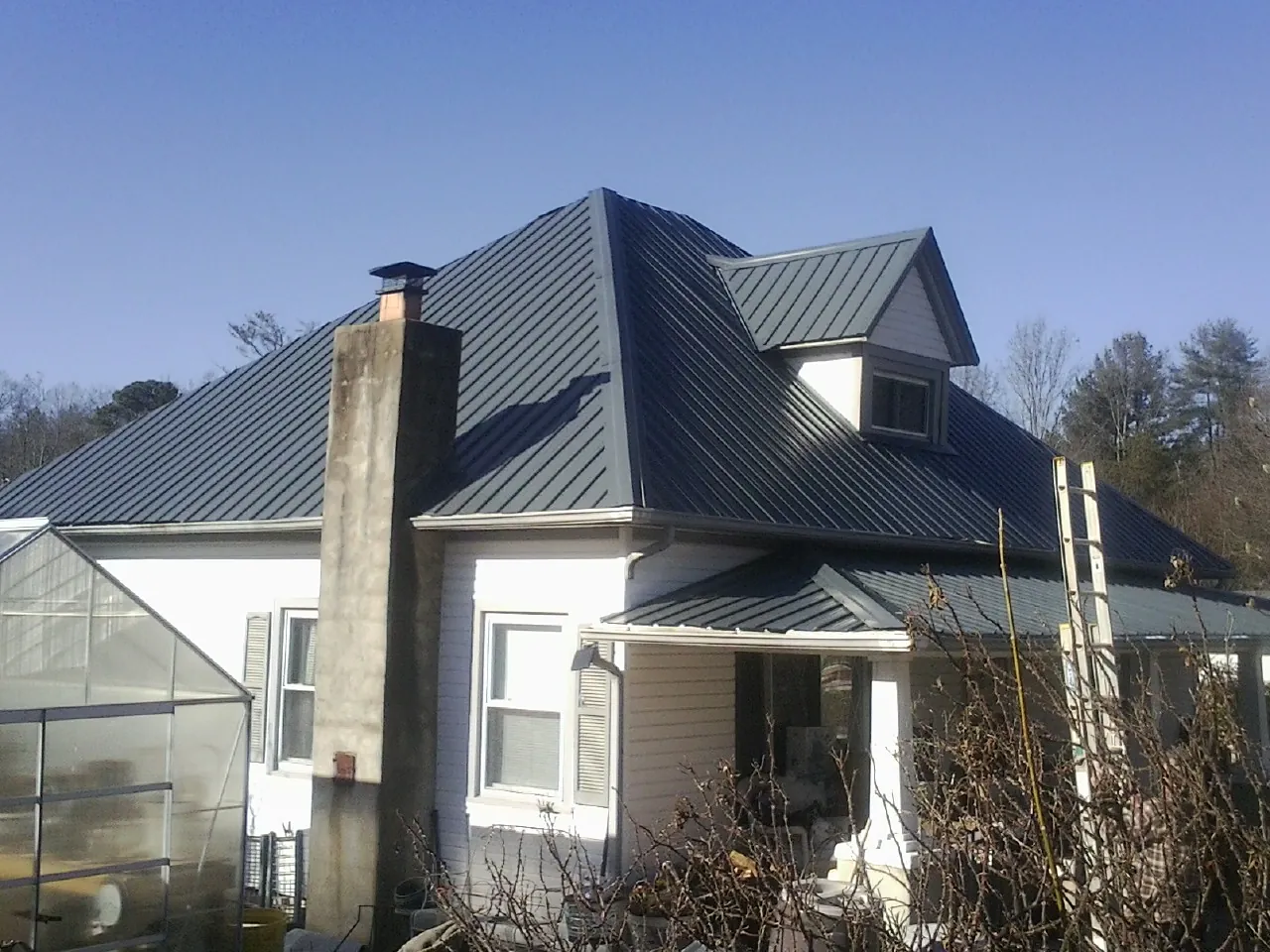 Dark blue standing seam metal roof on a white farmhouse with dormer — Slate & Tile Roof Repair by Roofing Brothers in Willow