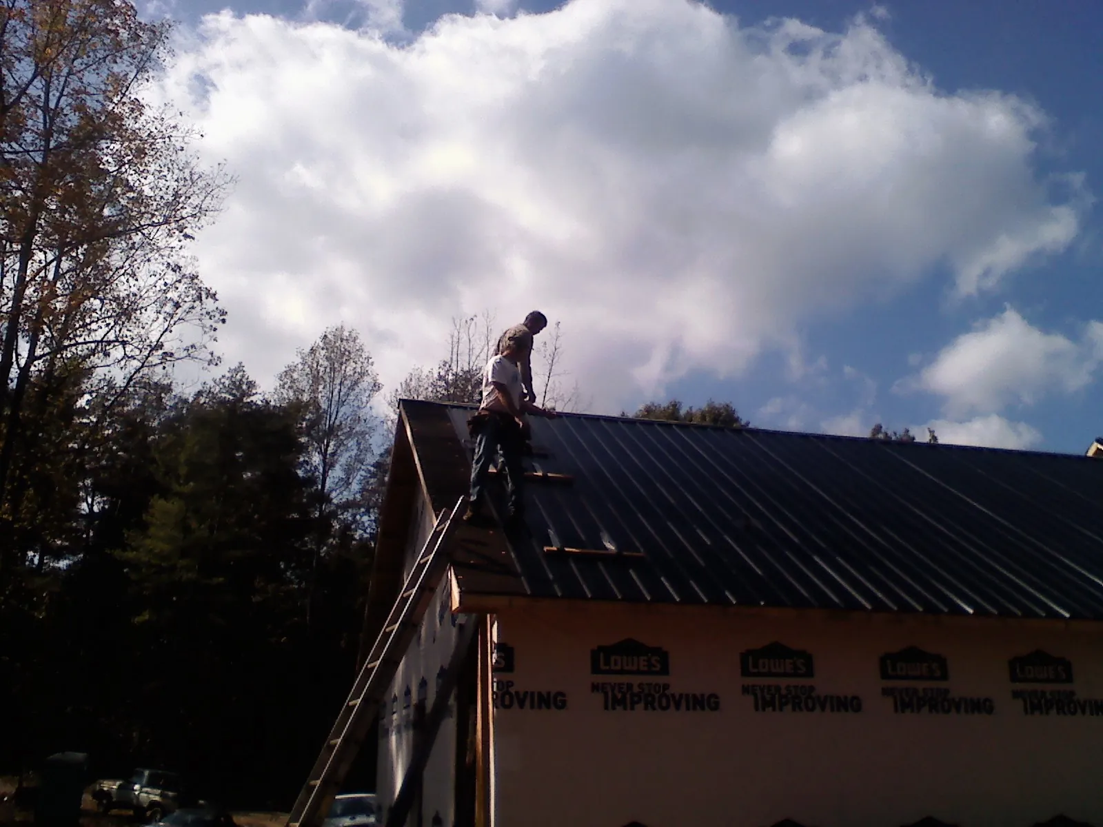Roofer fastening dark metal panels high against a cloudy sky, from a Roof Inspection job in Willow